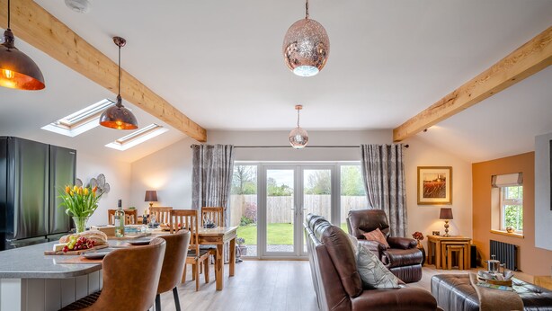 A modern kitchen with a dining area, a living room with a sofa, and a view of the garden through the glass door. - 2 bedroom accommodation in Pilling, near Preston (Pilling, near Preston)