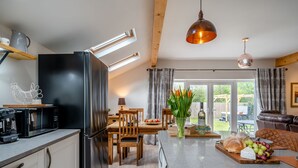 A modern kitchen with a built-in refrigerator, a microwave, and a coffee machine. There is a dining area with a wooden table and chairs, and a large window offering a view of the outdoors. - 2 bedroom accommodation in Pilling, near Preston (Pilling, near Preston)