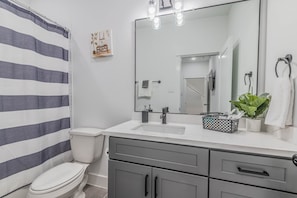 Une salle de bain moderne avec un lavabo blanc, des meubles gris, un grand miroir et un rideau de douche à rayures.