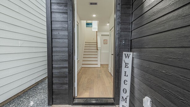 Un pasillo con una puerta de madera, un letrero de bienvenida y una escalera que conduce a un piso superior.