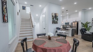 Una cocina moderna con armarios blancos, un refrigerador de acero inoxidable y un comedor con una mesa redonda y sillas.