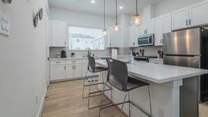 Una cocina moderna con gabinetes blancos, electrodomésticos de acero inoxidable e iluminación colgante.