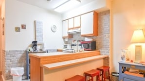 Una cocina compacta con una isla de madera, un microondas y un lavamanos. Hay tres taburetes en la isla.