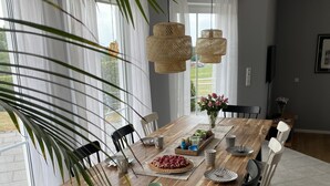 A dining area with a wooden table, white chairs, and a large window with sheer curtains. - Traumblick in die Natur (Hennef (Sieg))