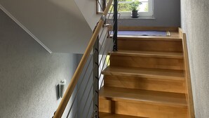 A wooden staircase with metal railings, leading to a landing with a window overlooking greenery. - Traumblick in die Natur (Hennef (Sieg))
