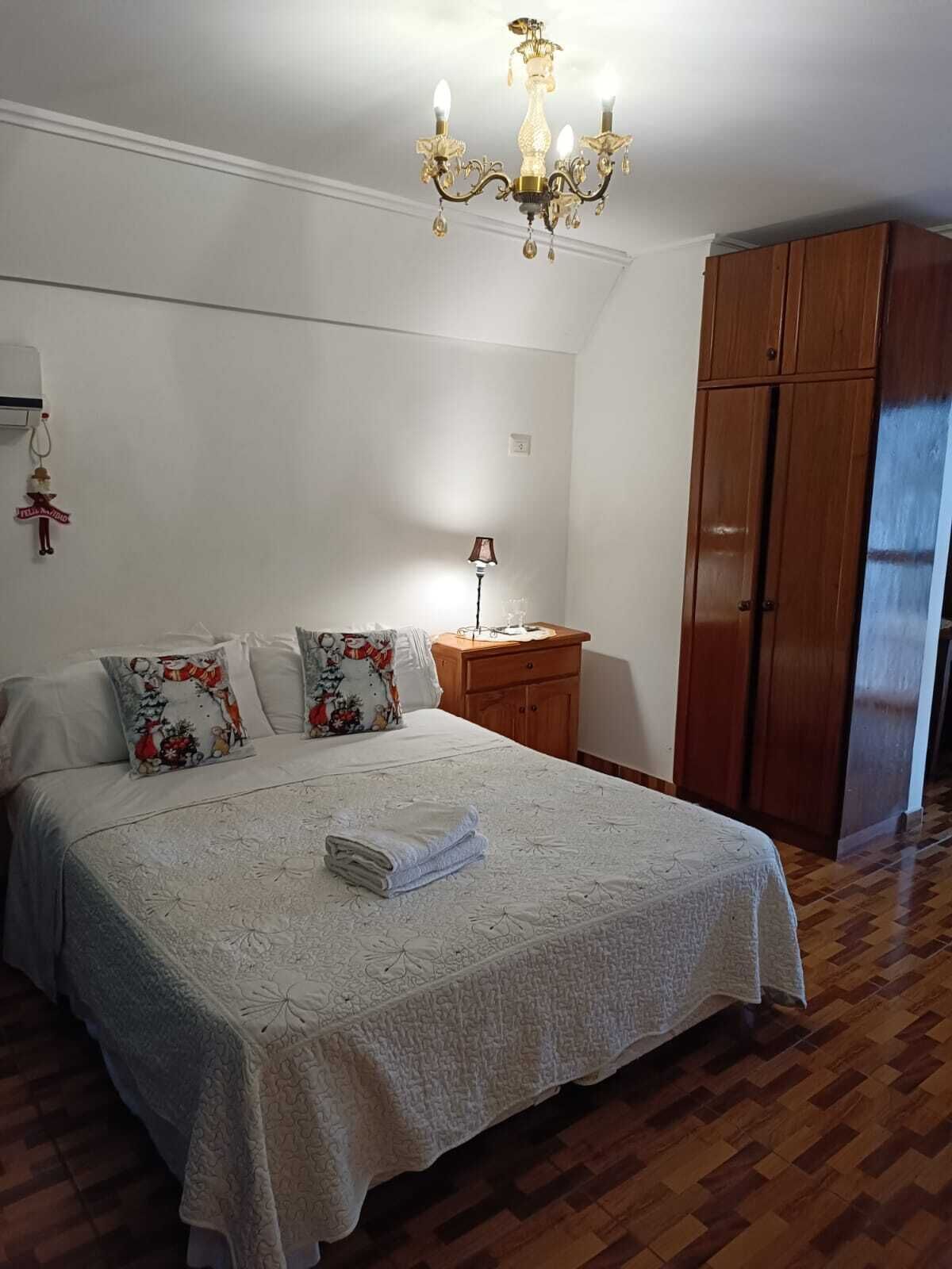 Un dormitorio con una cama grande, un armario de madera, una mesita de noche y una araña.