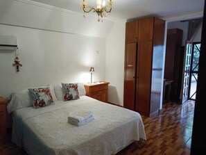 Un dormitorio con cama, mesitas de noche, una araña, armario de madera y vistas a través de una puerta.