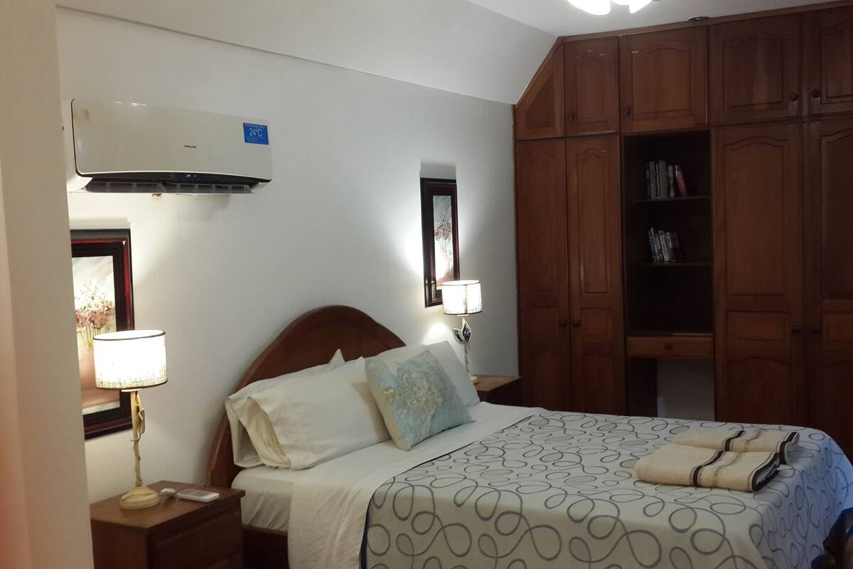 Een slaapkamer met een bed, nachtkastjes, een houten kledingkast en een airconditioner.