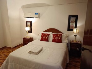 Una cama bien hecha con una toalla doblada, un cabecero de madera y dos mesitas de noche con lámparas.
