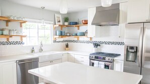 A modern kitchen with white cabinetry, a central island, stainless steel appliances, and wooden shelves. - Upscale Home w/ Private Yard (Oceanside)