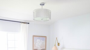A bedroom with a large bed, a bedside table, a chair, a hanging light fixture, and a window with curtains. - Upscale Home w/ Private Yard (Oceanside)