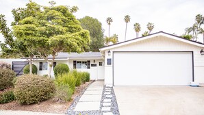 A modern house with a garage, surrounded by well-maintained landscaping and palm trees. - Upscale Home w/ Private Yard (Oceanside)