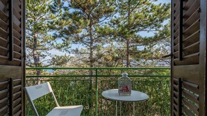 Un balcon avec une chaise blanche et une petite table ronde, une lanterne décorative et une vue sur des pins.