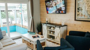 Un salon avec un téléviseur fixé au mur, un canapé, une table basse et une vue sur l’extérieur.