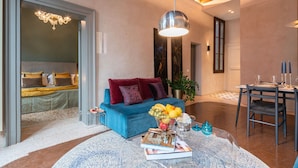 Un salon moderne avec un canapé bleu, un coin repas avec une table dressée pour deux personnes et un lustre.