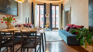 Un coin repas avec une table dressée pour quatre personnes, un canapé et une grande fenêtre avec des rideaux.