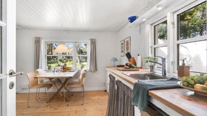 Eine kleine Küche mit Holztisch, zwei Korbstühlen, Spüle und Fenster mit Blick auf Grünflächen.