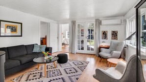 Ein modernes Wohnzimmer mit einem schwarzen Sofa, einem runden Couchtisch und einem grauen Sessel. Auf dem Boden liegt ein Teppich mit Muster, und an den Wänden befinden sich Kunstwerke.