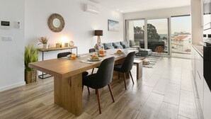 A modern living space with a dining area, a sofa, and a view of the city. - Sea & Sun Apartment - Pool with Sea View (Nazaré)