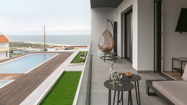 A balcony with a pool, a hanging chair, and a table with glasses and a bottle. - Sea & Sun Apartment - Pool with Sea View (Nazaré)