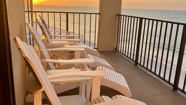 A balcony with white Adirondack chairs facing a sunset over the ocean. - January Special! - Remodeled condo on the beach super close to dining and hiking (Orange Beach)