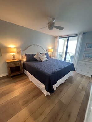 Une chambre à coucher avec un lit, deux tables de chevet avec des lampes, un ventilateur de plafond et un balcon avec vue.