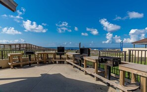 Une terrasse extérieure avec des bancs en bois et un espace barbecue, donnant sur une plage.