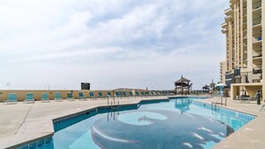 A swimming pool with a unique design, surrounded by lounge chairs and a building with balconies. - January Special! - Remodeled condo on the beach super close to dining and hiking (Orange Beach)