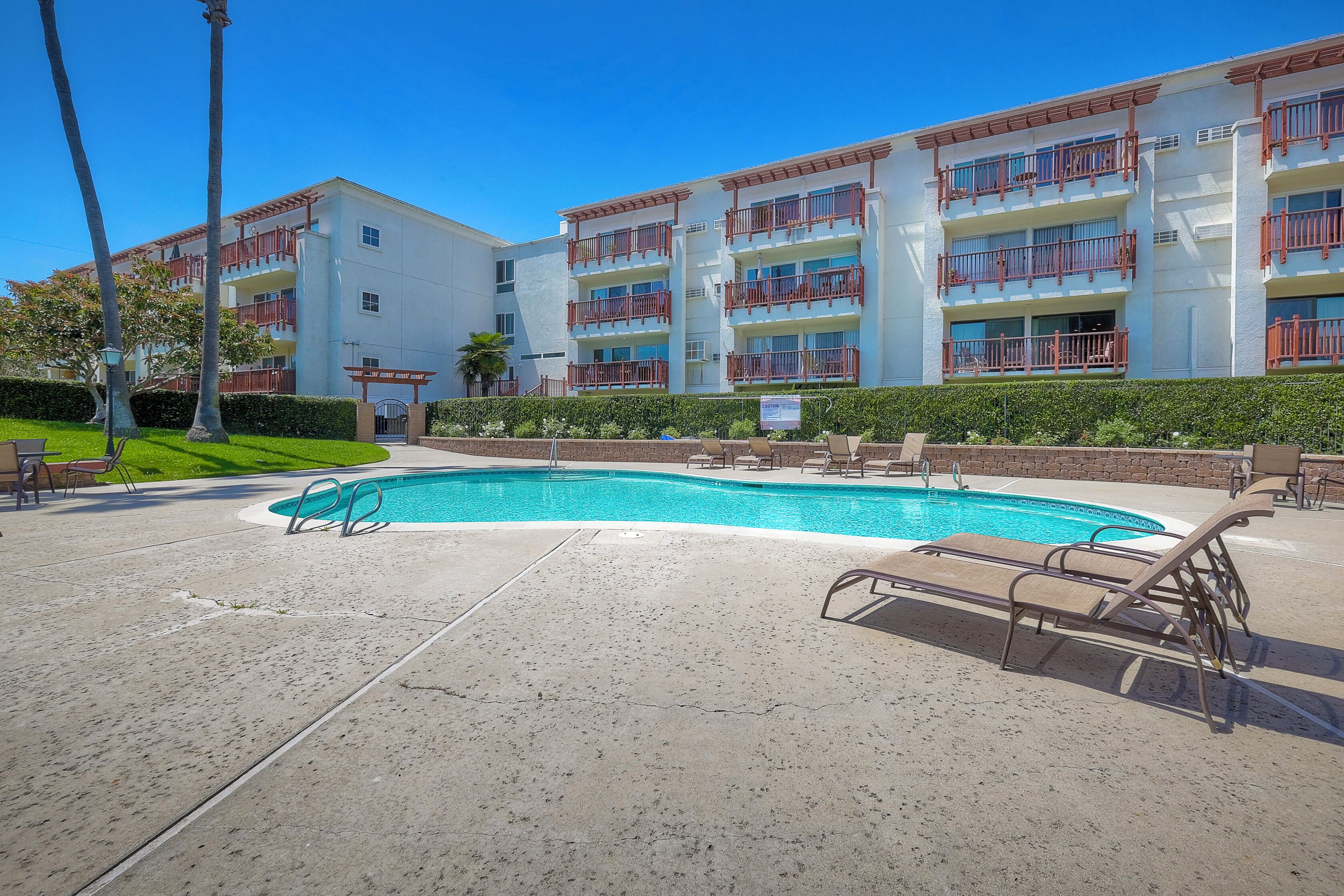 A hotel with a swimming pool, multiple balconies, and a well-maintained lawn.