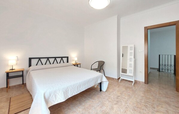 Een slaapkamer met een bed, twee nachtkastjes met lampen, een stoel, een garderobe en een deur die naar een andere kamer leidt.