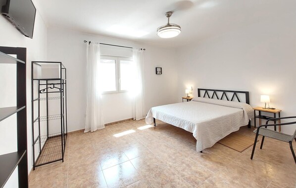 A bedroom with a bed, two bedside tables with lamps, a chair, a wardrobe, a ceiling fan, and a window with curtains. - 3 bedroom stunning home in Ador (Ador)