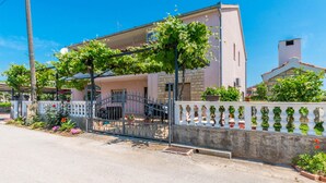 Une maison à deux étages avec un balcon, une entrée fermée par un portail et une clôture blanche.