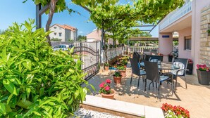 Une terrasse extérieure avec des tables et des chaises, entourée de plantes en pot et d’une clôture en métal.