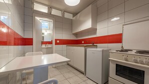 Una cucina compatta con mobili bianchi, uno schienale rosso, un frigorifero Siemens, un piano cottura Siemens e un lavandino piccolo.