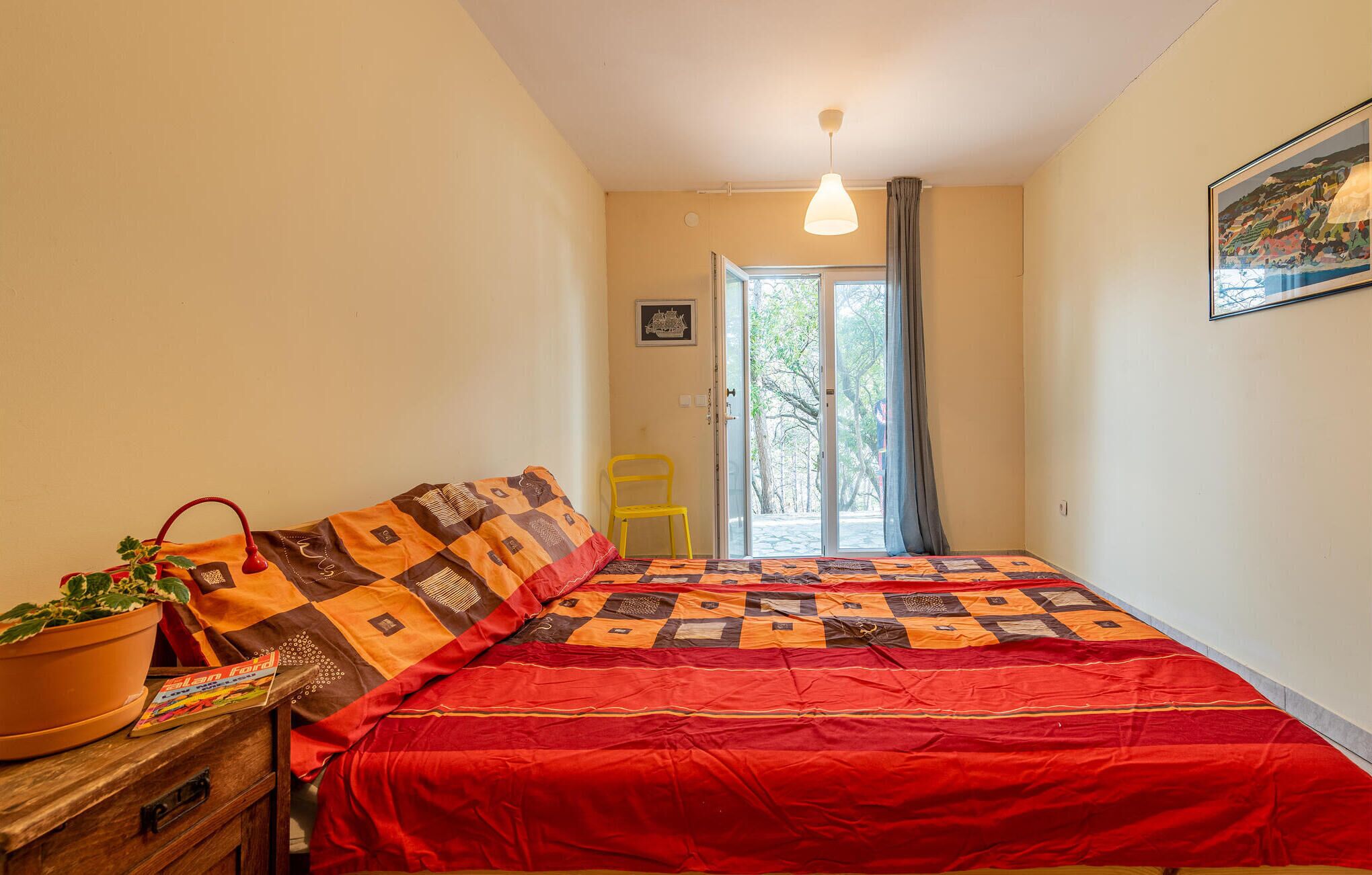 A bedroom with a bed, a chair, a potted plant, and a door leading to a balcony.
