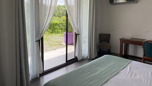 A hotel room with a bed, a desk, a chair, and a view of a garden through sheer curtains. - Nature rich home environment, minutes away from all state parks and beach towns. (Cahuita)