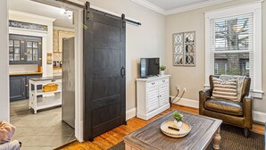 A living room with a sliding barn door, a television on a white cabinet, a leather armchair, and a coffee table with a decorative plate. - Nooga Nest - Charming 4BD, 2BA - 8 Mins From Downtown (Chattanooga)