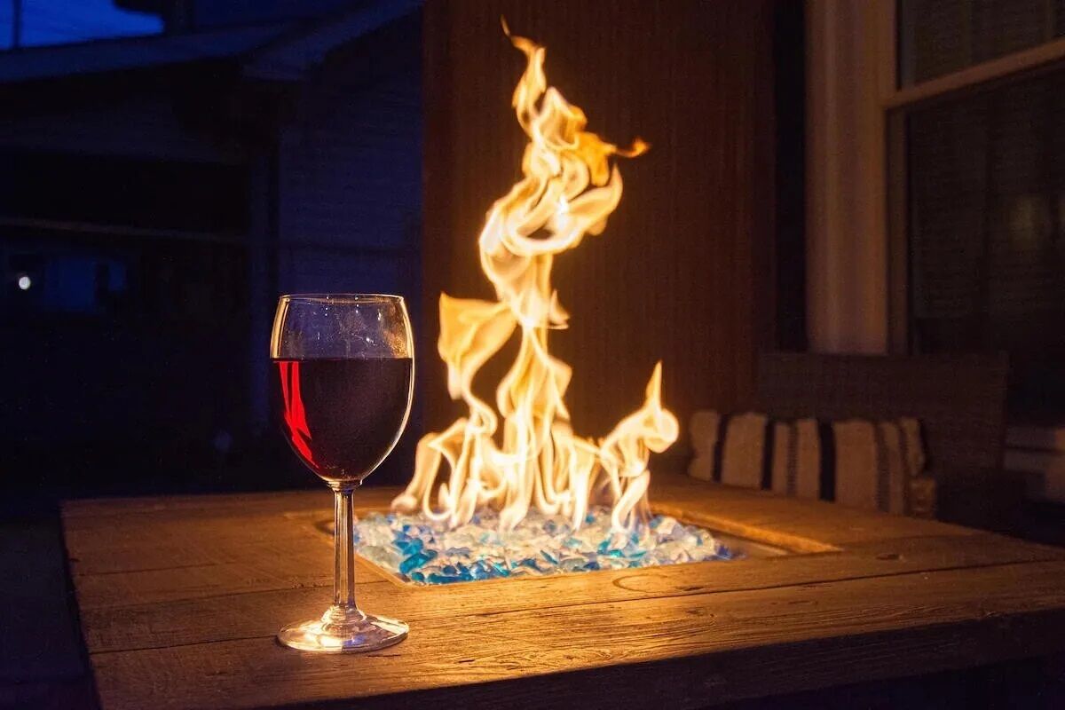 Una copa de vino tinto sobre una mesa de madera con una chimenea al fondo.