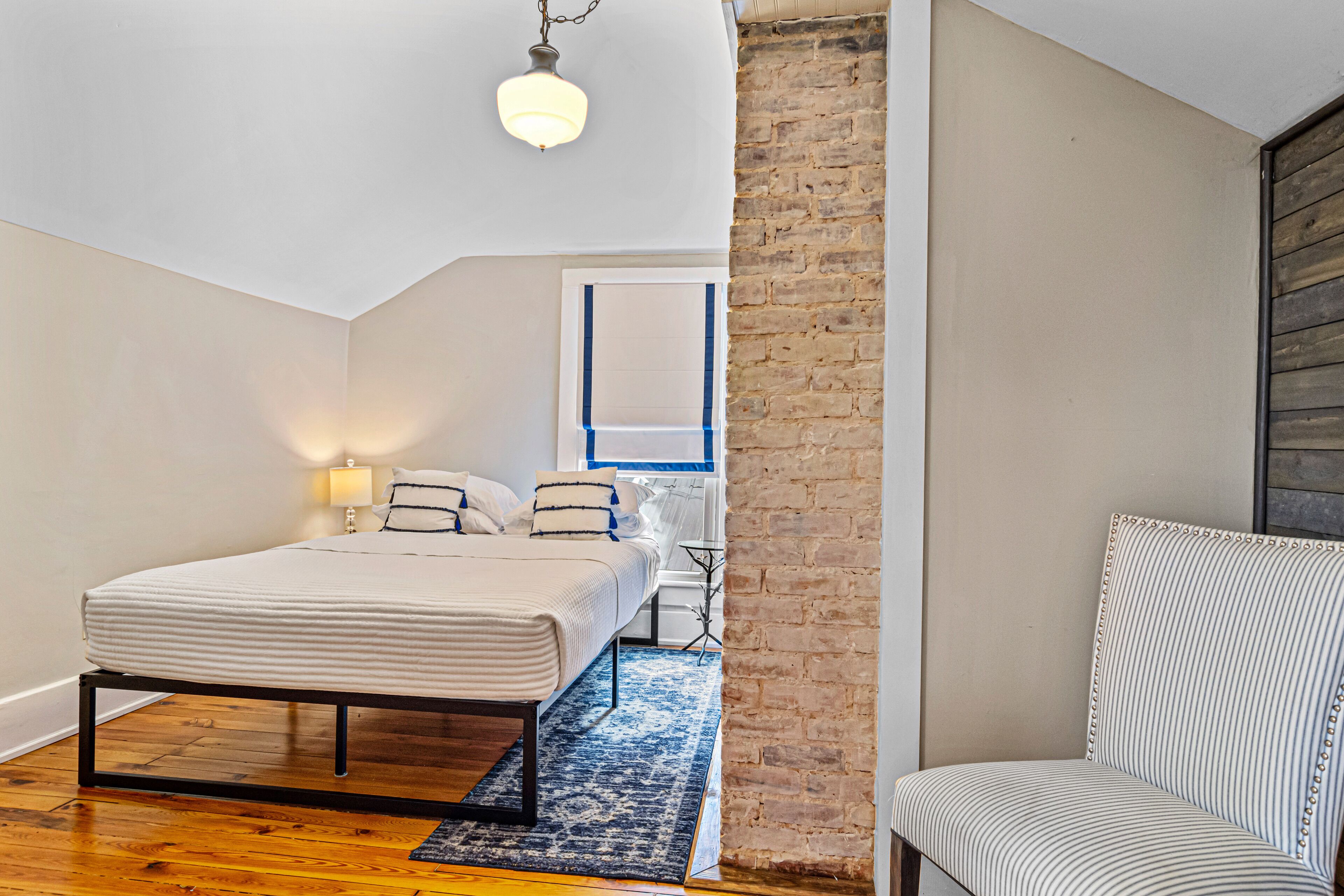 Une chambre à coucher avec un lit, une chaise, une lampe et un mur en briques.