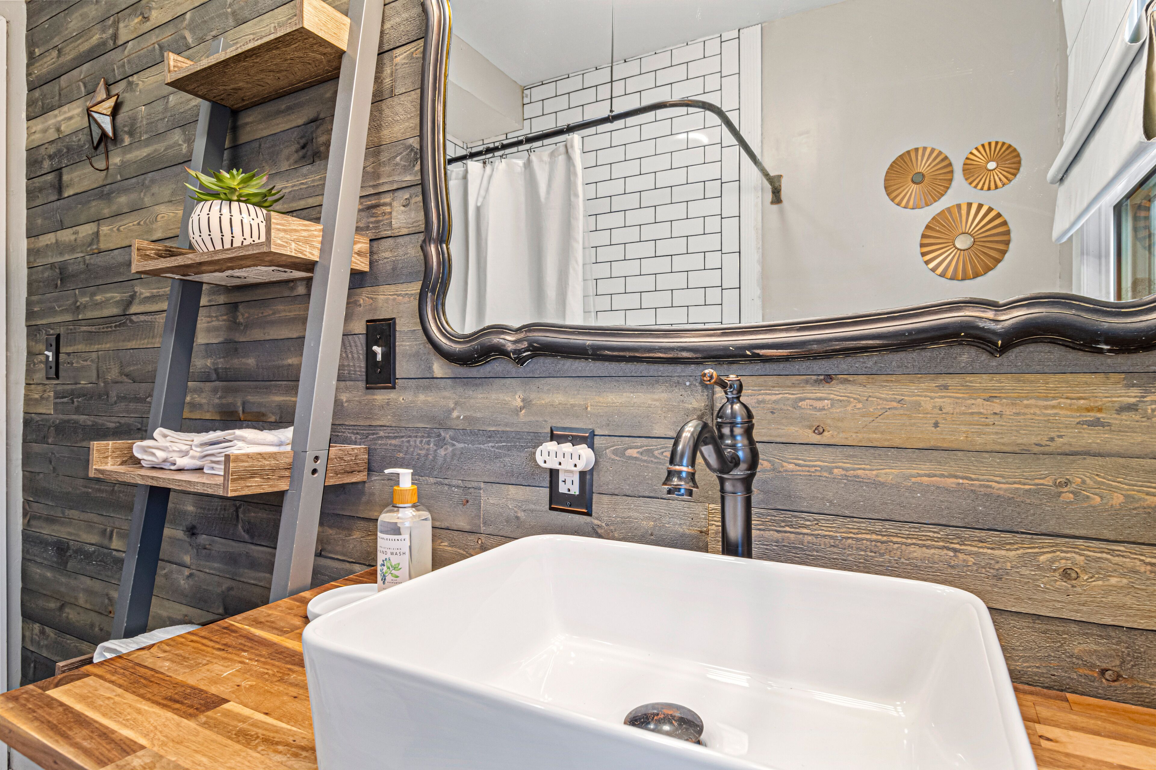 A bathroom with a wooden wall, a white sink, a mirror, and a shower curtain.