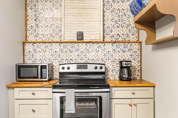 A kitchen with a microwave, stove, and coffee maker on a wooden countertop.