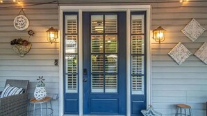 A front porch with a blue door, two wall-mounted lanterns, decorative wall art, wicker furniture, and a star-shaped decoration. - Nooga Nest - Charming 4BD, 2BA - 8 Mins From Downtown (Chattanooga)