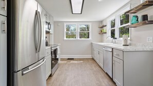A modern kitchen with stainless steel appliances, white cabinetry, and a window providing natural light. - Farmhouse Writer's Retreat in Historic Shepherdstown (Shepherdstown)