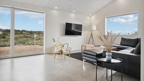 Una sala de estar moderna con un televisor grande, un sofá, una mesita de centro y vistas al exterior.