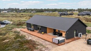 Una casa moderna con una terraza amplia, un jacuzzi y una zona de estar al aire libre techada.