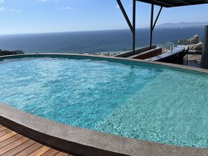 Uma piscina infinita azul cristalina com um deck de madeira, com vista para uma praia e oceano.