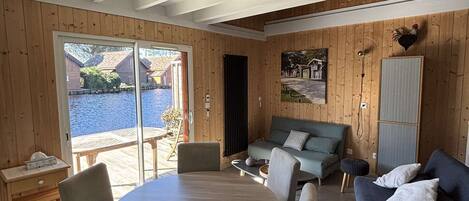 Un intérieur en bois comprenant une table à manger, des chaises, un canapé et une vue sur la mer grâce à de grandes fenêtres.