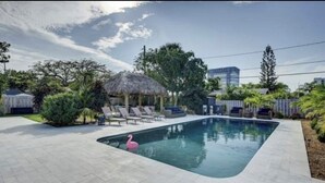 Una piscina con sillas de descanso y una estructura de techo de paja.