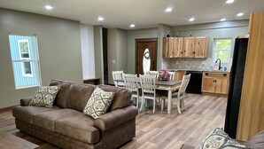 Uma sala de estar moderna com um sofá de couro marrom, almofadas decorativas estampadas e uma área de jantar com cadeiras brancas e uma mesa de madeira.