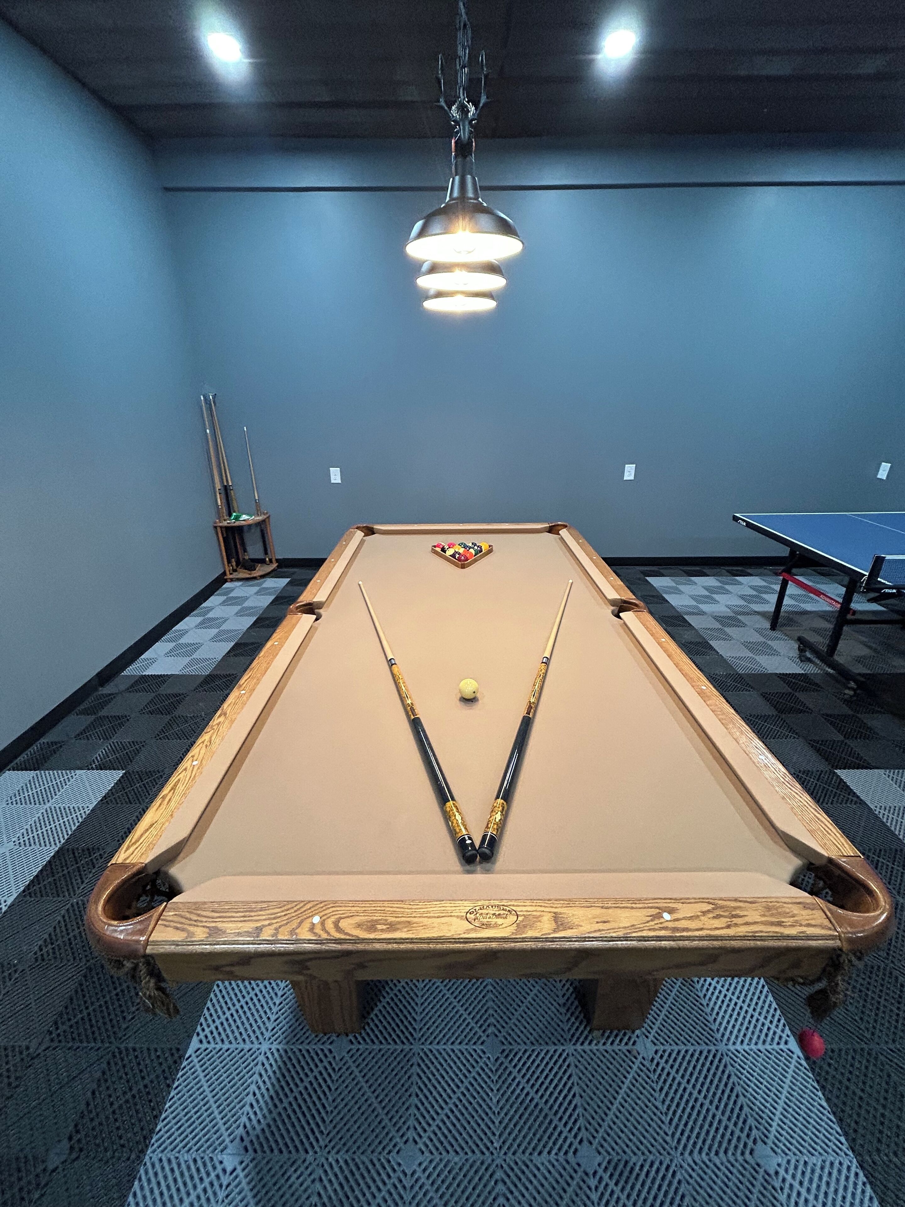A pool table with a cue ball, pool cues, and a pocket rack in a room with blue walls and a patterned carpet.